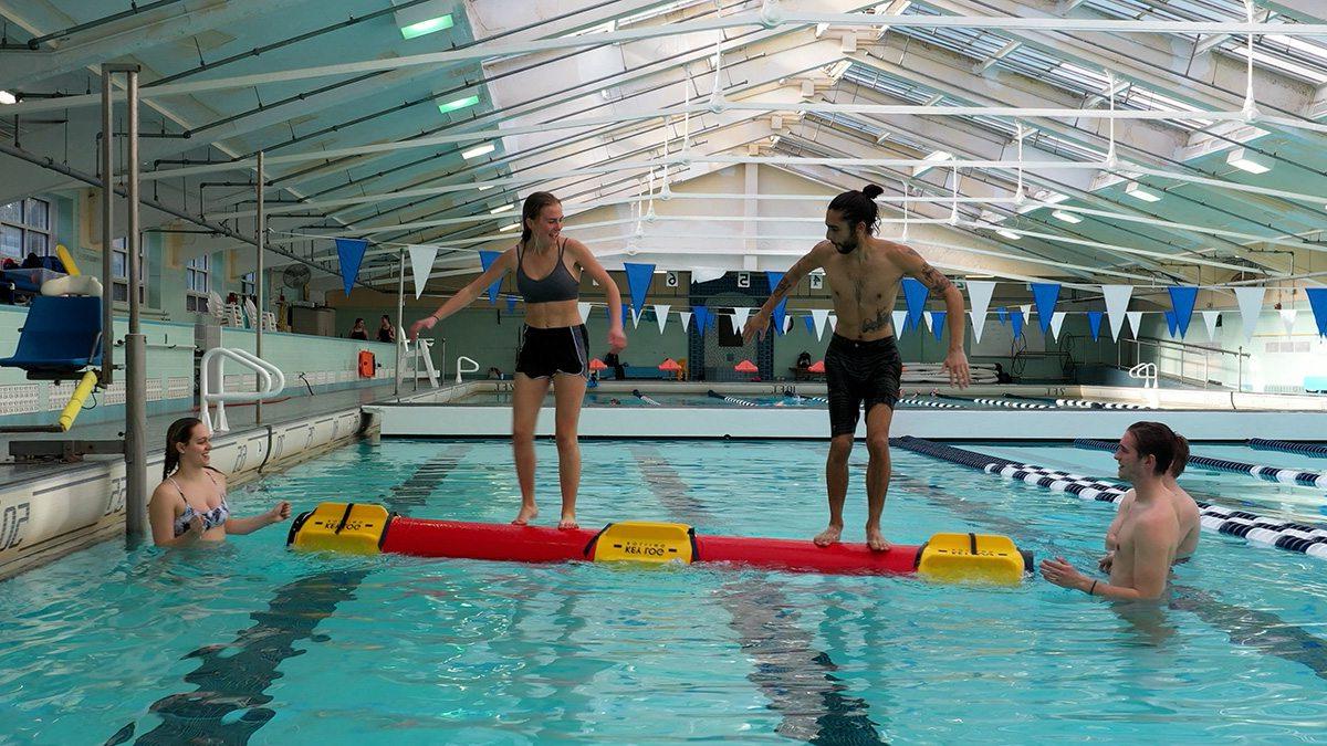 Two people on a Rolleo log in the pool.